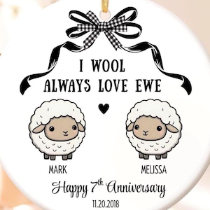 May include: A round white ceramic ornament featuring a black and white gingham bow at the top. The text reads I WOOL ALWAYS LOVE EWE above two cartoon sheep with the names MARK and MELISSA below them, followed by Happy 7th Anniversary 11.20.2018.