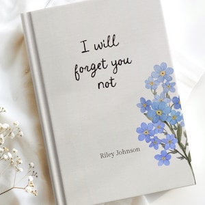 May include: A hardcover book with the text "I will forget you not" in black script. The book features a floral design of blue forget-me-nots and the author's name, Riley Johnson. The book is set against a white background.