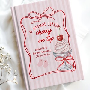 Op de afbeelding: Roze gastenboek voor een babyshower met een streepjespatroon. De cover heeft een rood kader met de tekst "a sweet little chewy on top" en een illustratie van een sundae met een kers. Het boek is voor Amelia's Babyshower op 20.08.2026.