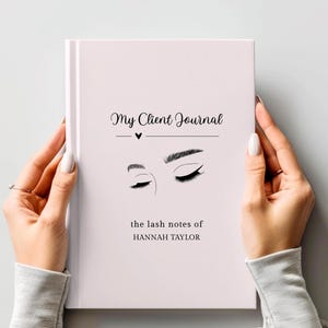Op de afbeelding: Een lichtroze notitieboek met de titel "My Client Journal" in zwarte tekst en een hartsymbool. Daaronder illustraties van wimpers en wenkbrauwen. De tekst "the lash notes of HANNAH TAYLOR" staat onderaan. Het notitieboek wordt door een persoon vastgehouden.