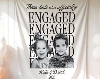 May include: A white fabric banner featuring the black text "These kids are officially ENGAGED" repeated in a grid pattern. A black and white photograph of a young girl and boy is centered, with the names "Kate & David" and "2026" printed below.