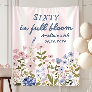 May include: A banner with the text "SIXTY in full bloom Amelia's 60th 06.20.2026" in blue script over a pink and white striped background. The bottom of the banner features a floral design with pink, blue, and purple flowers. White balloons and a gift box are also present.