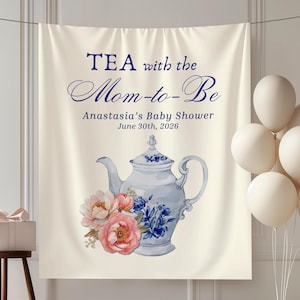 May include: A cream-coloured backdrop with the text "TEA with the Mom-to-Be" and "Anastasia's Baby Shower June 30th, 2026". A blue and white teapot with flowers is featured. White balloons and a gift box are also present.