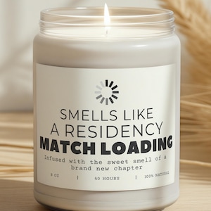 Può includere: Un barattolo di candela in vetro trasparente acceso con un'etichetta bianca. L'etichetta recita "SMELLS LIKE A RESIDENCY MATCH LOADING" con testo aggiuntivo. La candela è da 255 grammi e brucia per 40 ore. La candela è 100% naturale.
