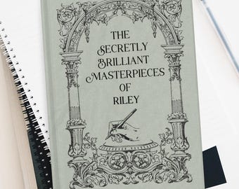 May include: A sage green hardcover journal featuring a black ink illustration of an ornate archway and a hand writing with a pen. The text reads THE SECRETLY BRILLIANT MASTERPIECES OF RILEY. The journal is placed atop a spiral notebook and a black folder.