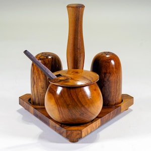 Può includere: Un set di sale e pepe in legno con zuccheriera e cucchiaio abbinati. Il set comprende due saliere e pepiere, una zuccheriera con coperchio e un cucchiaio, tutti in legno lucido. Il set è appoggiato su un vassoio triangolare in legno.
