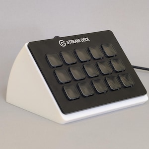 May include: A black and white Stream Deck with 15 illuminated buttons. The device has a white base and a black top with the words "STREAM DECK" printed on it. A black cable extends from the device.