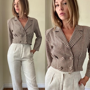 May include: A brown and white checkered blazer with a double-breasted design. The blazer is paired with light beige high-waisted pants. The outfit is a vintage style.