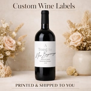 Può includere: Una bottiglia di vino scuro con un'etichetta bianca che recita "A Toast to New Beginnings". L'etichetta include anche il testo "cheers to Sarah Marketing Manager 2026". Le parole "Custom Wine Labels" sono in alto.