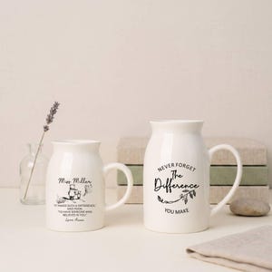 Puede incluir: Dos tazas de cerámica blanca con texto e ilustraciones en negro. Una taza dice "Miss Miller" con una ilustración de Winnie the Pooh y una cita. La otra taza dice "Nunca olvides la diferencia que haces". Un regalo reflexivo.