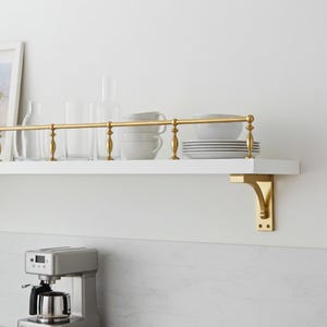 以下が含まれることがあります： 真鍮の手すりとブラケットが付いた白いフローティングシェルフ。白い食器、カップ、グラスが置かれています。シェルフは、ステンレス製のコーヒーメーカーの上にある白い壁に取り付けられています。シェルフの長さは約76cmです。