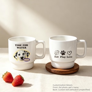 May include: Two white ceramic mugs with handles. The left mug features a Dalmatian dog image, the text "TIME FOR WATER," and the name "mimi." The right mug displays a bone, paw print, heart icon, and the text "Eat Play Love." Two strawberries sit nearby.