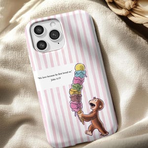 May include: A phone case with a pink and white striped design. It features a cartoon monkey holding a large ice cream cone with various coloured scoops. The case includes the text, "We love because he first loved us." John 4:19.