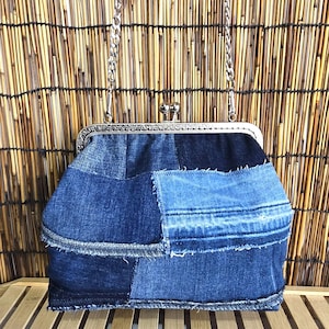 Può includere: Una borsa a mano patchwork in denim con una tracolla a catena argentata e una chiusura a scatto in metallo. La borsa è realizzata con varie tonalità di denim blu, creando un aspetto unico e strutturato. La borsa è su una superficie di legno.