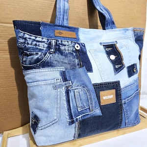 Puede incluir: Un bolso tote de mezclilla patchwork con varios tonos de azul. La bolsa presenta múltiples bolsillos, cremalleras y una etiqueta Weekday. Las asas están hechas del mismo material de mezclilla.