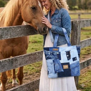 May include: A tote bag constructed from various shades of blue denim fabric patches, featuring visible seams, pockets, and metal buttons. The bag has two sturdy denim shoulder straps and a rectangular brown leather-like label on the front panel.