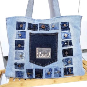 May include: Light blue denim tote bag with a dark blue denim pocket and patches. The bag features a rectangular pocket with the text "PEPETTO JEANS". Patches with buttons and zippers are sewn onto the bag.