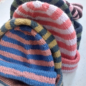 Puede incluir: Una colecci&oacute;n de gorros de punto coloridos. Los gorros presentan rayas horizontales en varias combinaciones de colores, incluyendo azul y rosa, coral y blanco, y verde y negro. Los sombreros est&aacute;n hechos de un hilo suave y texturizado.