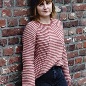 Pode incluir: Um suéter listrado rosa e branco com mangas compridas e gola redonda. O suéter é feito de um tecido macio e de malha.