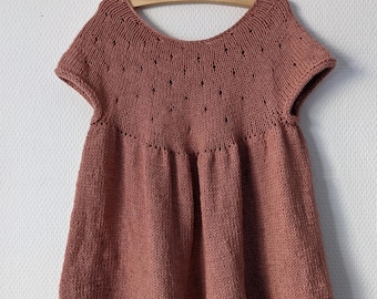 Könnte beinhalten: Ein gestricktes Babykleid in staubigem Rosaton mit kurzen Ärmeln und einem gewellten Saum.