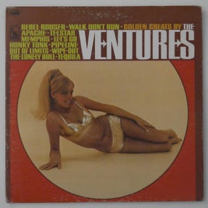 May include: Vintage vinyl record album cover for "Golden Greats by The Ventures." The cover features a woman in a gold bikini, lying down in a circle against a red background. The album title and song titles are printed on the cover.