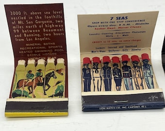 May include: Two vintage matchbook covers. The left cover features a colorful illustration of two people riding horses with the text "3000 ft. above sea level nestled in the foothills of Mt. San Gorgonio, two miles north of highway 99 between Beaumont and Banning, two hours from Los Angeles. Mineral Baths Recreational Sports Heated Swimming Pool Saddle Horses American Plan". The right cover features a black and white illustration of eight people in uniform with the text "7 Seas Shop with one stop convenience Open every day: 8 A.M. - Midnite Locker Dept. Never Closes Laundry - Cleaning - Alterations - Photostats While - Walt CREDIT in 10 min, no extra charges Lockers: Insured and Sanitized Men's Wear - Uniforms - Gifts - Jewelry LION MATCH CO., INC. CARTERET, N.J."