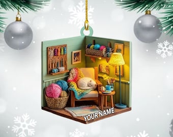 May include: A Christmas ornament featuring a cozy miniature room with a sleeping white cat on a chair. The room includes yarn, a lamp, and a basket of yarn. The ornament has the text "YOUR NAME" on the rug.