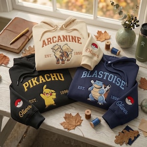 Può includere: Tre felpe con cappuccio in crema, nero e blu navy con personaggi Pokemon ricamati Arcanine, Pikachu e Blastoise. Ogni felpa mostra il nome del personaggio, l'anno 1996 e un polsino della manica personalizzato con il nome Oliver.