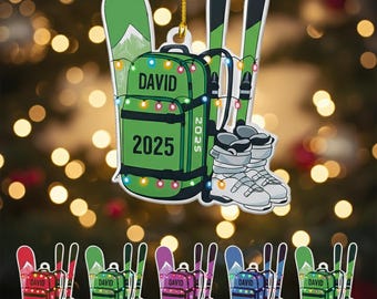 Peut inclure: Ornement de Noël représentant un sac à dos vert avec le nom "DAVID" et l'année "2025", des skis et des chaussures de ski. Il est orné de guirlandes lumineuses. Plusieurs variations de couleurs sont présentées.