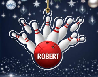 Puede incluir: Adorno navideño con temática de bolos. Presenta una bola roja con el nombre "ROBERT" y bolos blancos con rayas rojas. El adorno cuelga de un hilo dorado sobre un fondo azul oscuro con copos de nieve.
