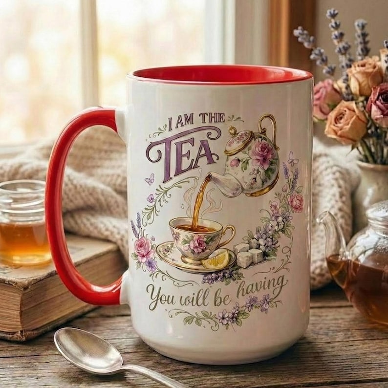May include: A large white ceramic mug with a red interior and handle. The mug features a floral design with a teapot pouring tea into a teacup, and the text "I AM THE TEA You will be having."