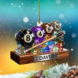 Peut inclure: Ornement décoratif sur le thème du billard, avec trois boules de billard numérotées 8, 4 et 9, et une queue. L'ornement a une base en bois avec une plaque signalétique en métal qui dit "DAVID". Les boules sont dans un style vitrail.