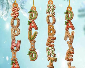 Puede incluir: Adornos navideños de pan de jengibre que deletrean los nombres Sophia, David, Robert y Daniel. Cada letra está decorada con glaseado y diseños festivos, colgando de hilos dorados sobre un fondo nevado.