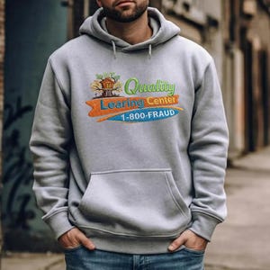 Könnte beinhalten: Ein grauer Kapuzenpullover mit einer Vordertasche. Der Pullover hat ein gesticktes Design mit den Worten "Quality Learning Center" und der Telefonnummer "1-800-FRAUD" in einem farbenfrohen Design. Das Design beinhaltet eine Baumhaus-Grafik.