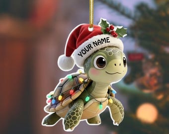 May include: A festive Christmas tree ornament shaped like a cartoon turtle. The turtle wears a red Santa hat with the text "YOUR NAME". It is adorned with fairy lights and holly, suspended by a gold string.
