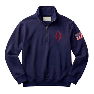 May include: Navy blue pullover sweatshirt with a quarter-zip closure and a stand-up collar. Features a red monogram on the chest and a small American flag patch on the sleeve. The sweatshirt is made of a soft, comfortable material.
