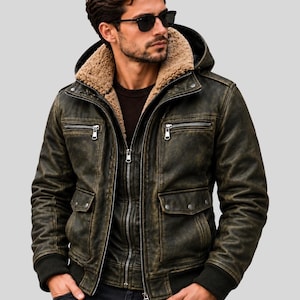 Op de afbeelding: Een verweerde donker olijfgroene leren jas met een beige imitatiebont voering, een afneembare capuchon, twee borstzakken met rits, twee onderste klepzakken met drukknopen en geribbelde boorden. De jas heeft een ritssluiting aan de voorzijde.