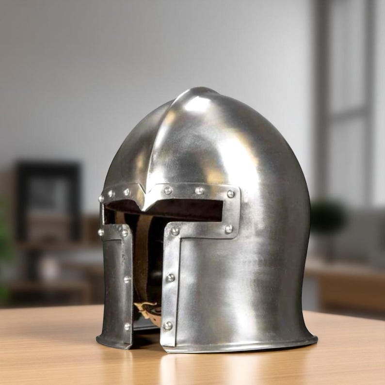 K&ouml;nnte beinhalten: Ein polierter, silberfarbener Metallhelm mit genieteten Details. Der Helm hat eine abgerundete Oberseite und eine Gesichts&ouml;ffnung mit rechteckigen Augenschlitzen. Es ist wahrscheinlich ein historischer oder mittelalterlicher Helm.