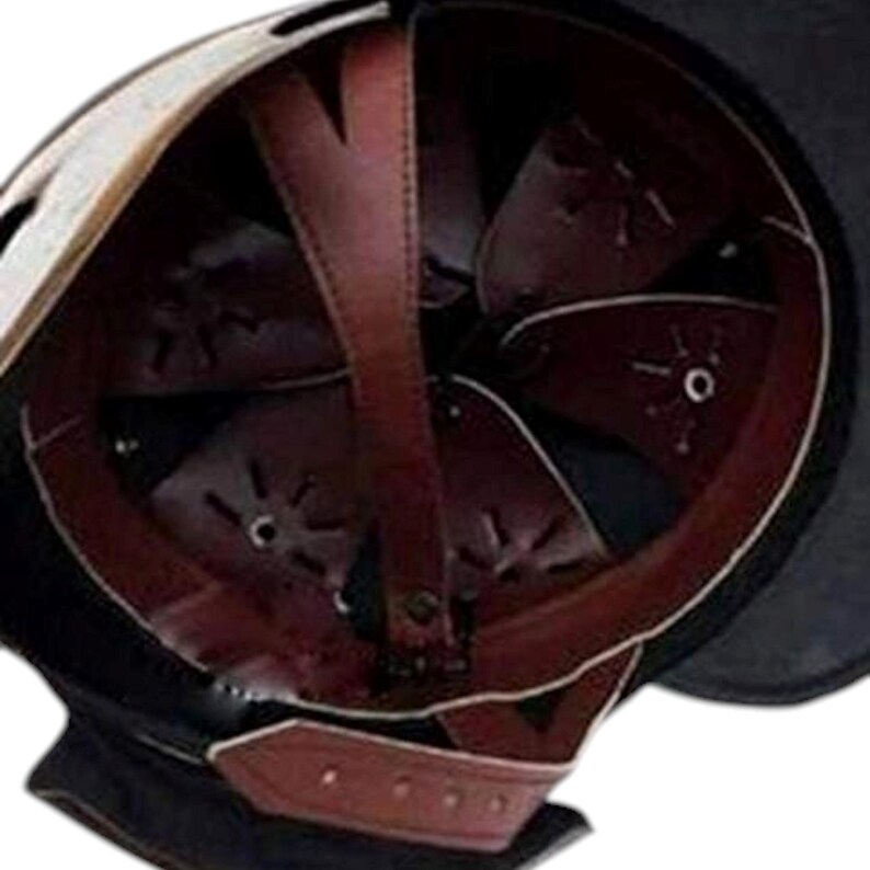 Puede incluir: Vista de cerca del interior de un casco negro y marr&oacute;n. El casco presenta un forro y correas de cuero marr&oacute;n oscuro, con un exterior negro y un ribete blanco. El acolchado interior es visible y el casco parece ser de metal.