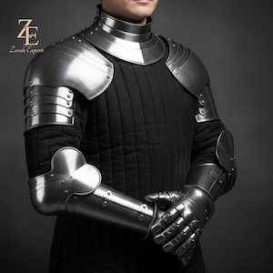 Könnte beinhalten: Eine silberfarbene mittelalterliche Rüstung, einschließlich eines Gorgets, Schulterstücke und gegliederten Armabwehr. Die Rüstung ist genietet und wird über einem schwarzen, gesteppten Kleidungsstück getragen. Das Bild enthält das Logo "Zurah Exports".