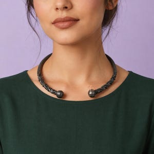 May include: A dark gray, oxidized metal choker necklace featuring a twisted, rope-like texture throughout the band. The necklace is an open-ended design, terminating in two smooth, spherical ball ends that face each other at the center of the neck.