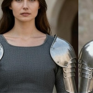 May include: A set of polished steel pauldrons featuring a multi-layered articulated design with visible rivets. The shoulder armor is worn over a grey long-sleeved garment, showcasing a metallic finish and a structured, protective construction.