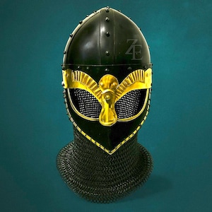 May include: A black medieval helmet with gold accents and a chainmail neck guard. The helmet features a gold faceplate with a stylized bird design and the initials "ZE" on the crown. Rivets secure the helmet's construction.