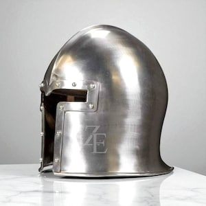 K&ouml;nnte beinhalten: Ein polierter silberfarbener Metallhelm mit abgerundeter Oberseite und rechteckiger Augen&ouml;ffnung. Nieten sichern das Visier. Der Helm hat die eingravierten Buchstaben "ZE" auf der Vorderseite. F&uuml;r historische Nachstellung oder Ausstellung.