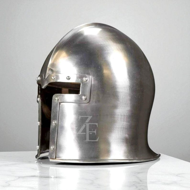 K&ouml;nnte beinhalten: Ein polierter silberfarbener Metallhelm mit abgerundeter Oberseite und rechteckiger Augen&ouml;ffnung. Nieten sichern das Visier. Der Helm hat die eingravierten Buchstaben "ZE" auf der Vorderseite. F&uuml;r historische Nachstellung oder Ausstellung.