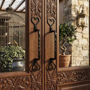 May include: A pair of double wooden doors featuring intricate floral carvings and black metal handles with heart-shaped ends. The doors have glass panels reflecting a birdcage with birds, a potted plant, and a wall-mounted outdoor lantern.