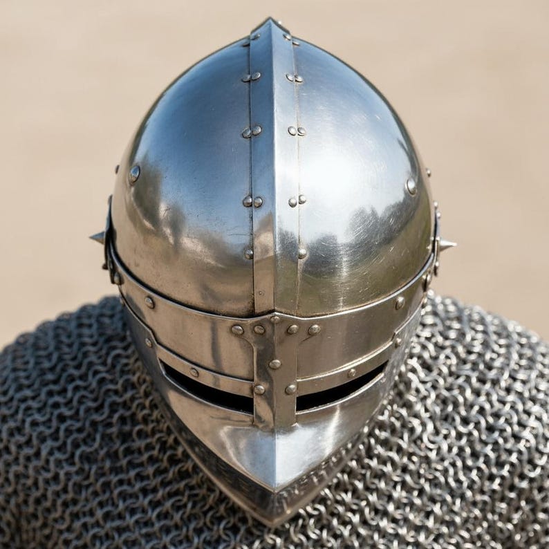 May include: A polished, silver-colored medieval helmet with riveted construction and a pointed top. The helmet features a face guard and is worn over a chainmail coif. The design suggests historical reenactment or costume use.