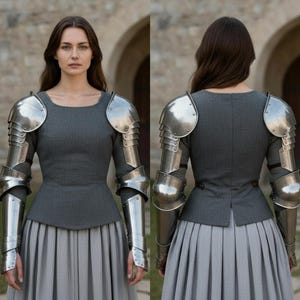 May include: A grey long-sleeved top paired with a matching pleated skirt and polished steel plate armor covering the shoulders and arms. The armor features articulated metal segments extending from the shoulder pauldrons down to the forearm guards.
