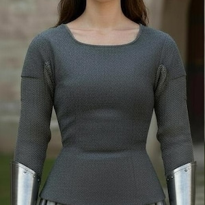 May include: A long-sleeved charcoal gray textured top with a scoop neckline, paired with a light gray pleated skirt. The garment features metallic silver forearm bracers worn over the sleeves, extending from the wrists to the mid-forearm area.
