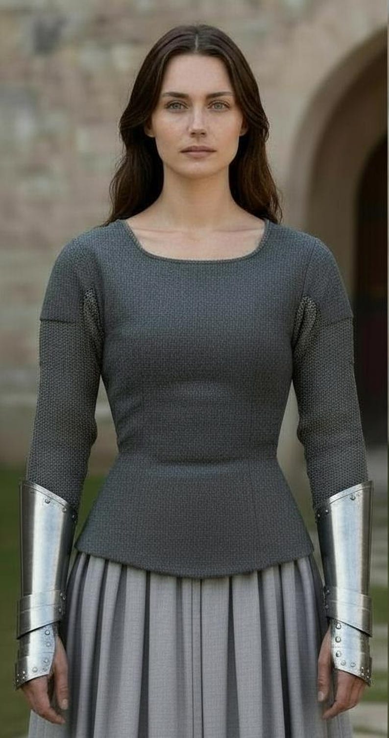 May include: A long-sleeved charcoal gray textured top with a scoop neckline, paired with a light gray pleated skirt. The garment features metallic silver forearm bracers worn over the sleeves, extending from the wrists to the mid-forearm area.